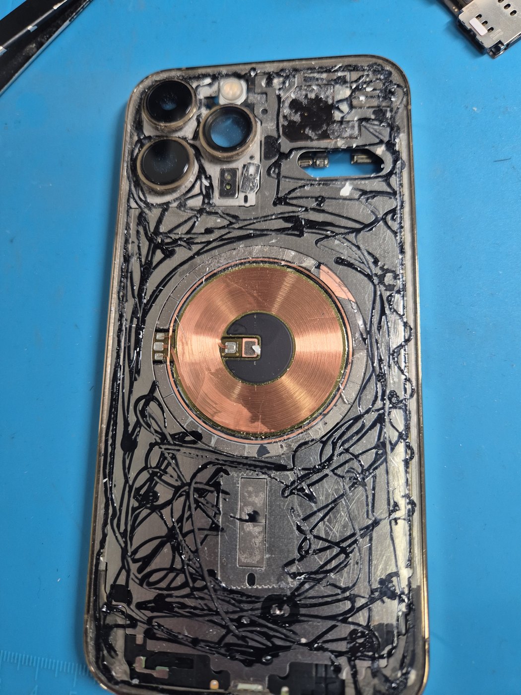 Damaged iPhone back housing before repair on a blue mat